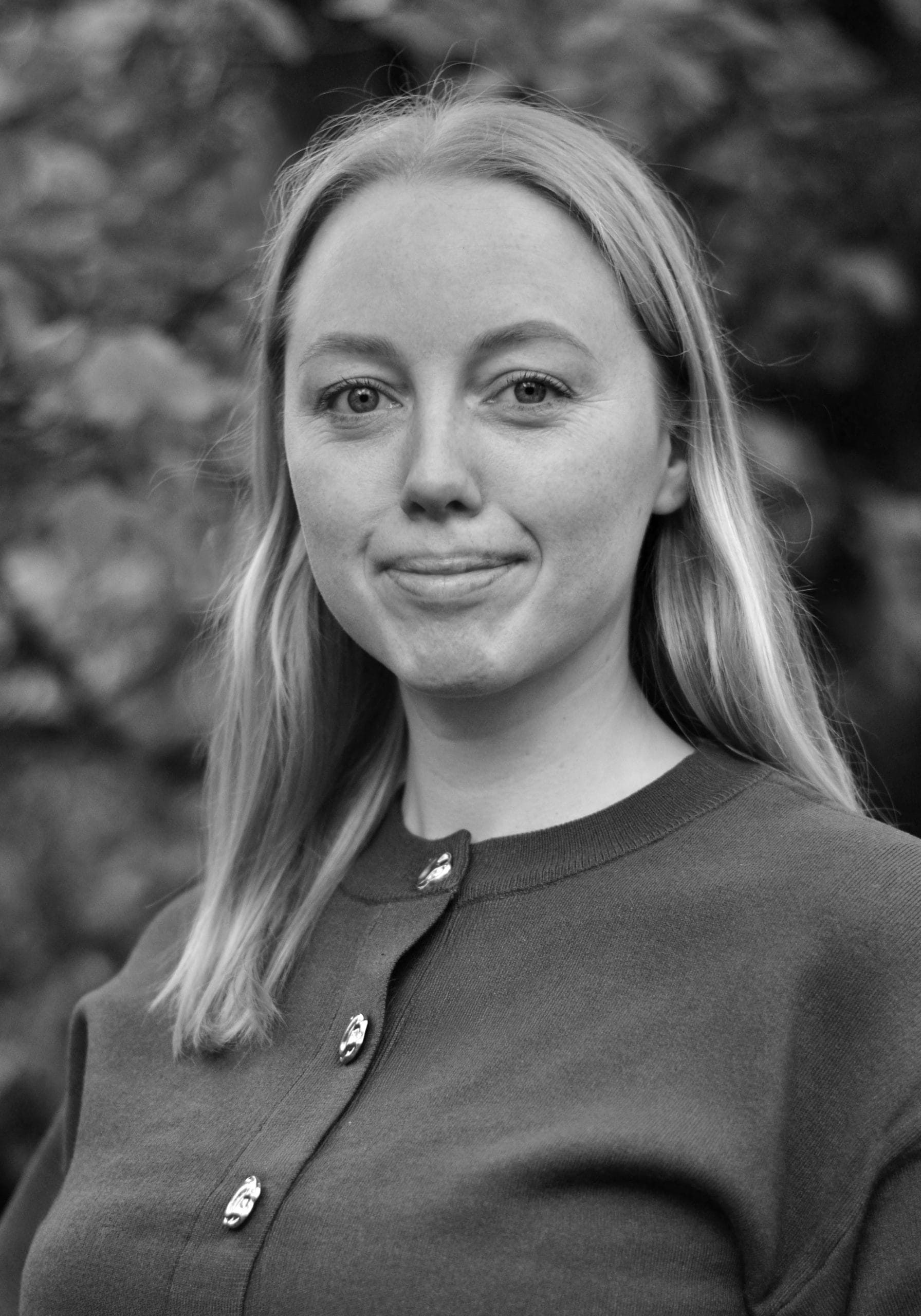 svart-hvitt bilde av kvinne med halvlangt lyst hår, smiler til kamera.